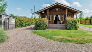 A wooden cabin with a porch, gravel driveway, and surrounding greenery.