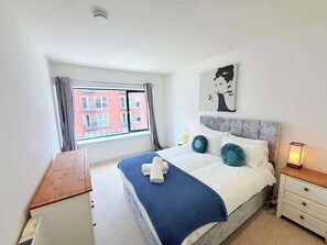 Ein Hotelzimmer mit einem großen Bett, einem Nachttisch, Vorhängen an einem Fenster und Blick auf Gebäude.