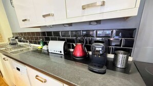 Et køkken med hvide skabe, en backsplash med sorte fliser, en kaffemaskine, en rød elkedel og en sigte i rustfrit stål.