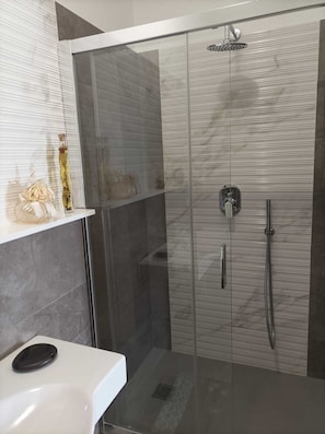 Une salle de bain moderne avec une douche à parois de verre, un lavabo blanc et des objets décoratifs disposés sur une étagère.