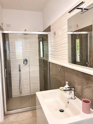 Une salle de bain moderne avec une douche à parois de verre, un lavabo blanc et un grand miroir au-dessus du lavabo.