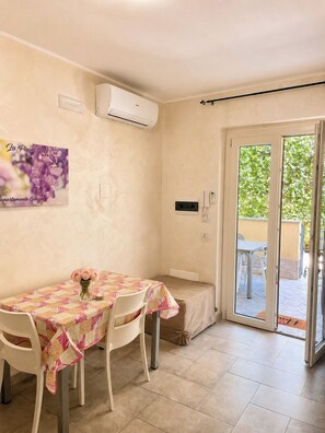 Une pièce comprenant une table et des chaises, une porte-fenêtre coulissante donnant sur un espace extérieur et un climatiseur fixé au mur.