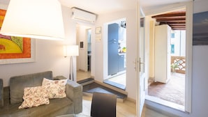 Una sala de estar con sofá, lámpara y puerta que da a una cocina.