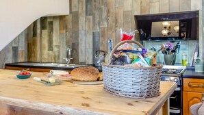 Une cuisine avec un plan de travail en bois, un panier de pain, un saladier de fruits et une bouteille de vin.