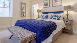 A bedroom with a bed, a bench, a bedside table, a lamp, and framed pictures on the wall. - 2 Bed in Bideford (oc-77589) (Northam)