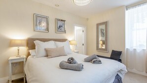 Una cama bien hecha con almohadas y toallas enrolladas, una mesita de noche con lámpara y un espejo grande en la pared.