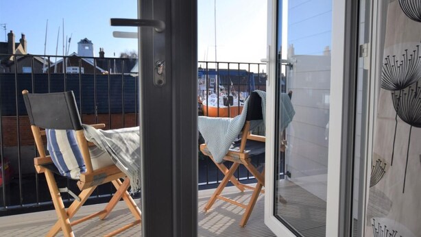 Un balcón con dos sillones de madera, uno con un cojín a rayas y el otro con una manta gris.