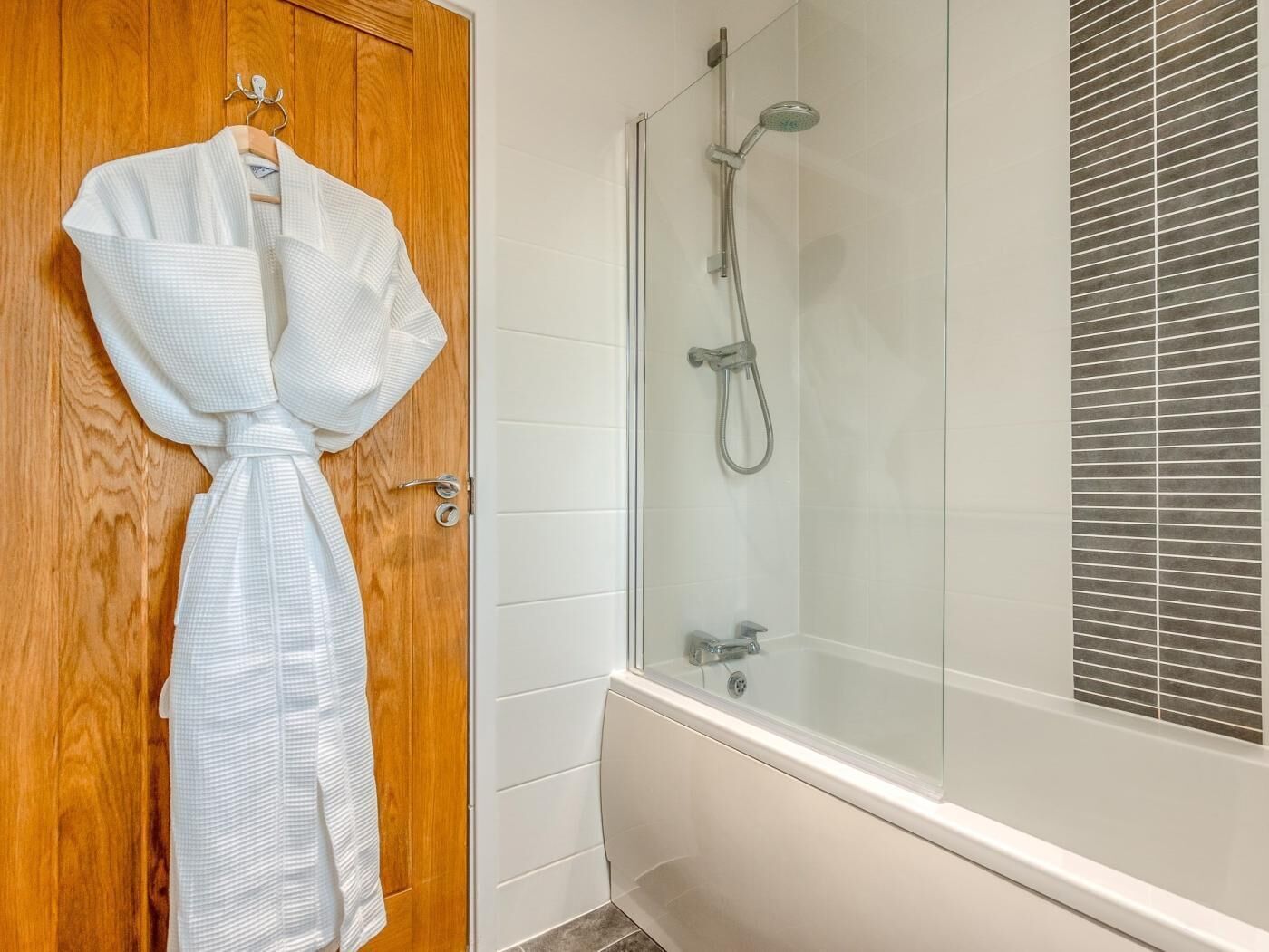 Un baño con puerta de madera, una bañera blanca y una zona de ducha con mampara de cristal.