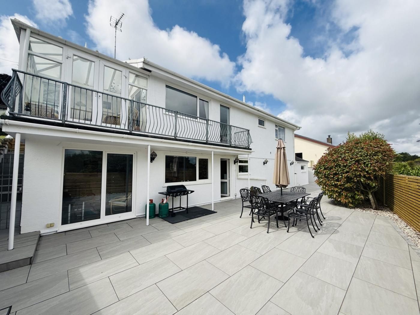 A two-story house with a balcony, a patio with outdoor furniture, and a large window.