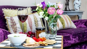 Uma mesa de jantar com uma taça de vinho tinto, um vaso com flores, um pote de mel e diversos petiscos.