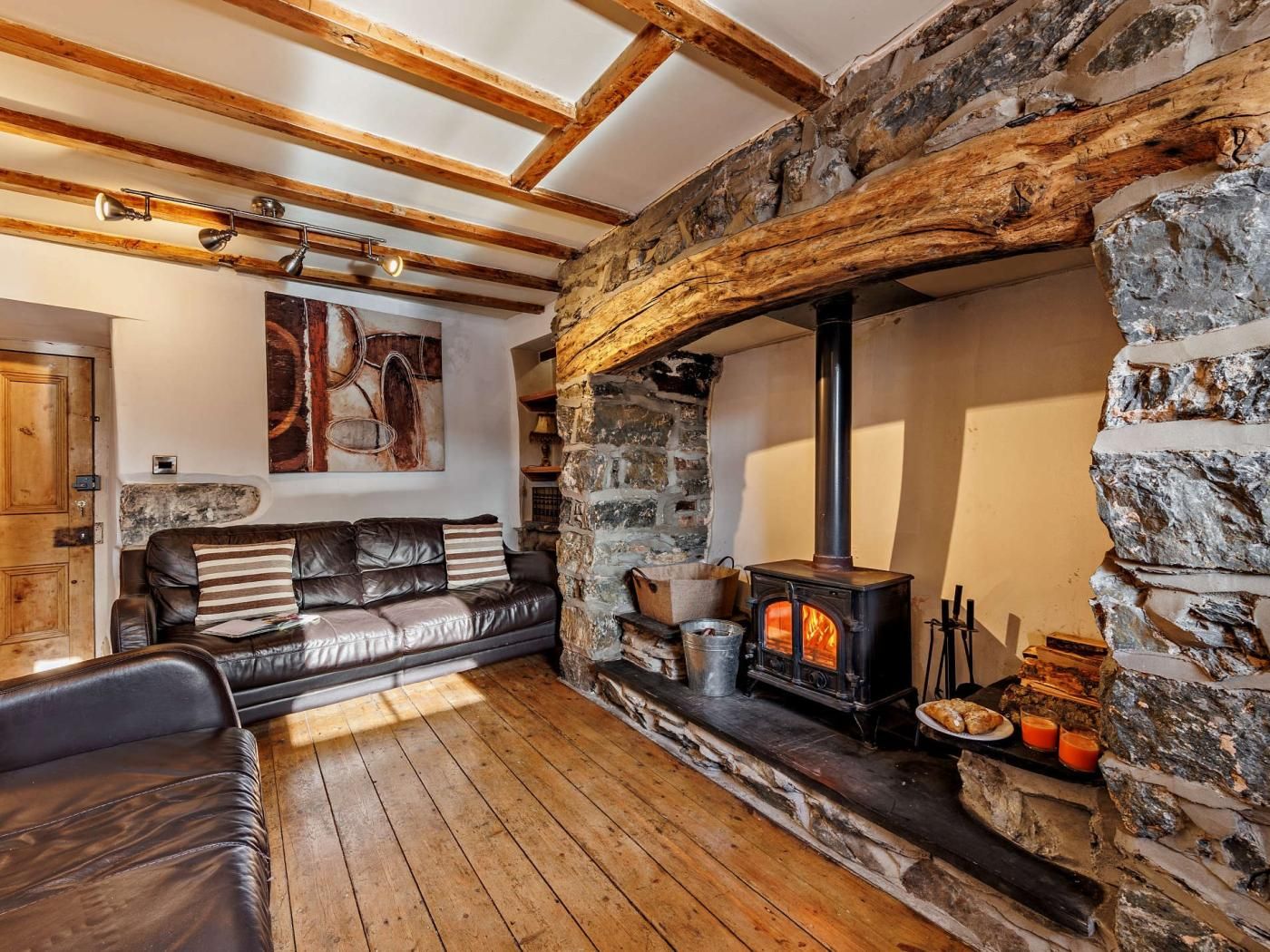 A cozy living room with a stone fireplace, a leather sofa, and a wooden ceiling.