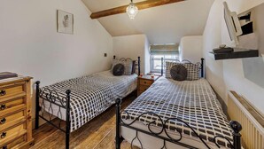 Een slaapkamer met twee bedden, houten lades, een radiator en een plafondlamp.