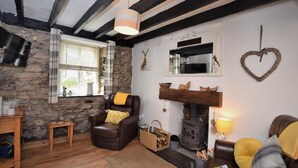 A cozy living room with a stone wall, a fireplace, a leather armchair, and a wooden floor. - 1 Bed in Caernarfon (oc-77891) (Llanaelhaearn)