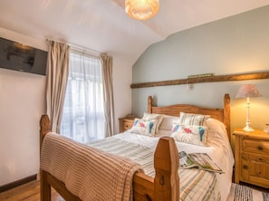 A bedroom with a wooden bed, a bedside table, a lamp, and a wall-mounted TV. - 1 Bed in Caernarfon (oc-77891) (Llanaelhaearn)