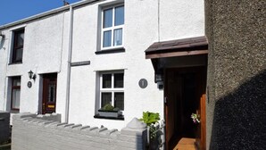 A two-story building with a white exterior, numbered doors, and a small window with a planter. - 1 Bed in Caernarfon (oc-77891) (Llanaelhaearn)