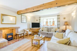 A cozy living room with a fireplace, sofa, TV, and wooden ceiling beams. - 4 Bed in Melton Constable (oc-77924) (Briston)