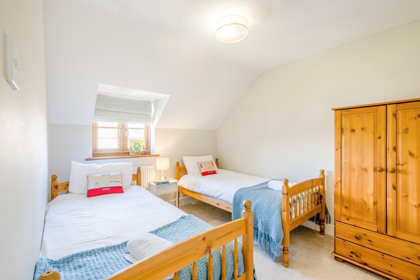 Quarto com duas camas, um guarda-roupa de madeira, uma janela com cortinas e uma luminária no teto.