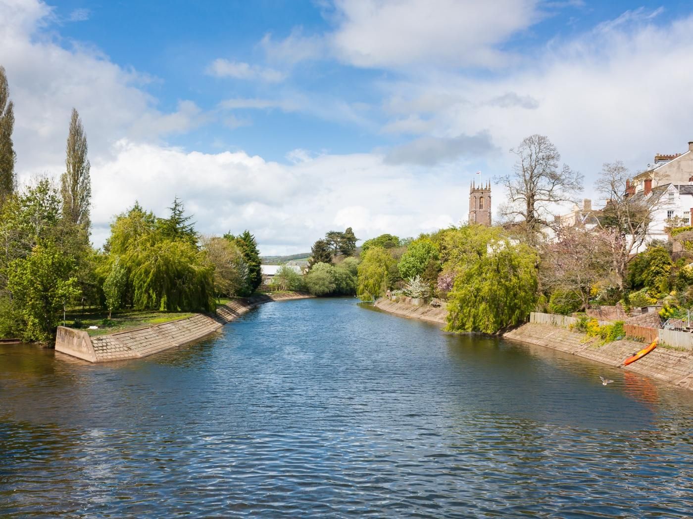 Ein Fluss mit einer Brücke, Bäumen und einer Kirche im Hintergrund.