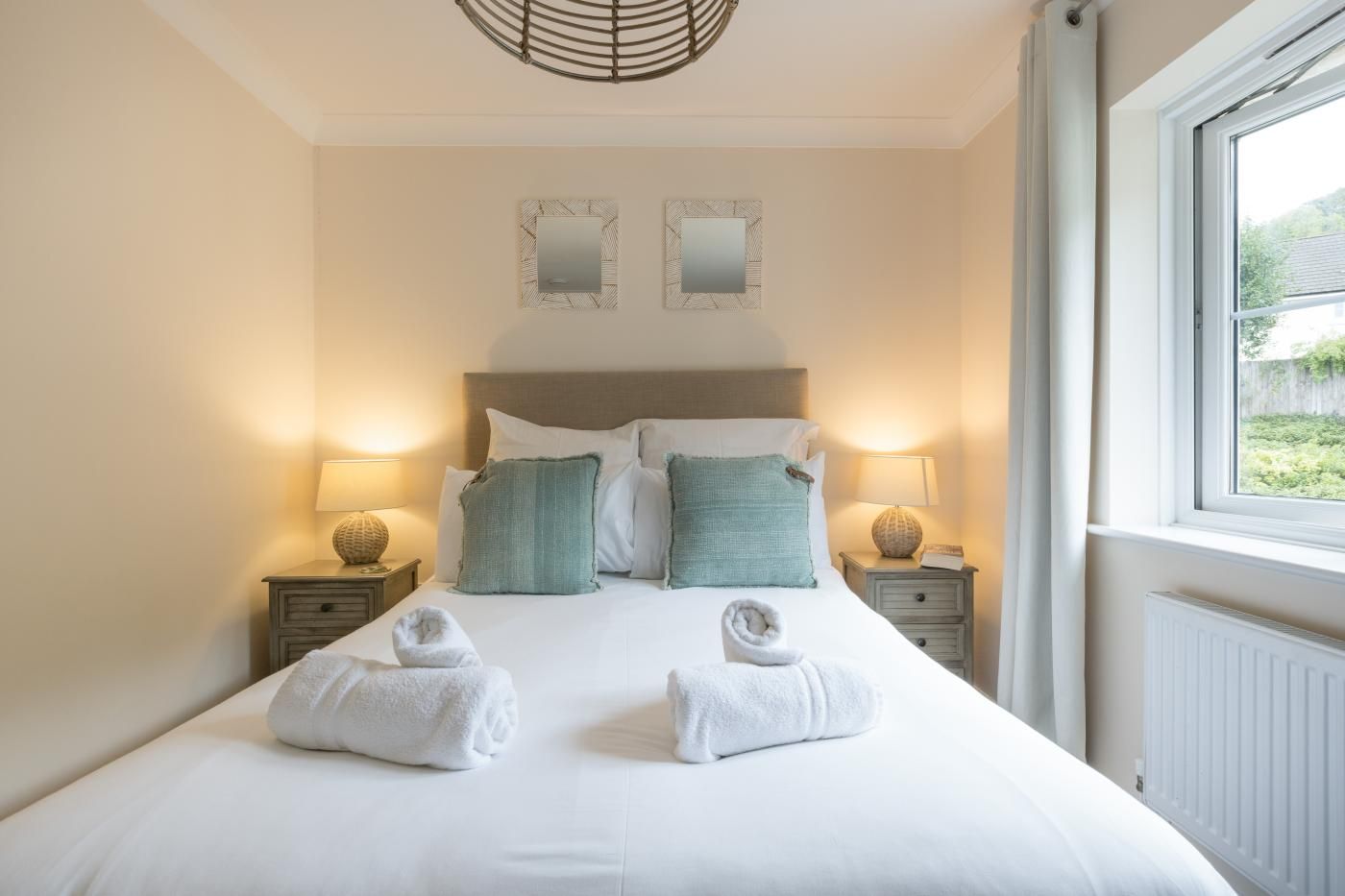 A hotel room with a large bed, two bedside tables with lamps, a headboard, and two wall mirrors.