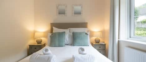 A hotel room with a large bed, two bedside tables with lamps, a headboard, and two wall mirrors.
