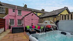 Un jacuzzi con agua corriente, una casa rosa y una valla de madera.