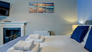 Habitación de hotel con cama, dos toallas, chimenea, televisor montado en la pared y un cuadro de una playa.
