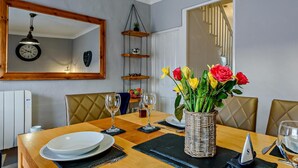Un comedor con mesa de madera, sillas, un florero y un reloj en la pared.