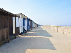 A row of beachside wooden structures with benches, a concrete walkway, and a sandy beach. - 4 Bed in Mablethorpe (oc-77958) (Mablethorpe and Sutton)