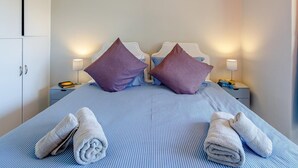 Quarto de hotel com cama, duas mesas de cabeceira, um guarda-roupa e uma luminária em cada mesa.