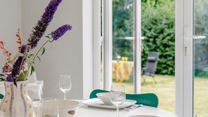 Uma mesa de jantar com um vaso de flores roxas, um copo e uma tigela.
