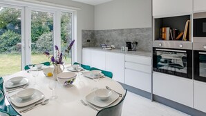 Uma cozinha moderna com armários brancos, um painel de parede cinza e uma área de jantar com uma mesa posta para seis pessoas.
