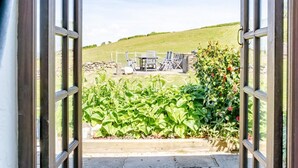 Une porte ouverte donne sur un patio aménagé avec du mobilier d’extérieur et un mur en pierre.