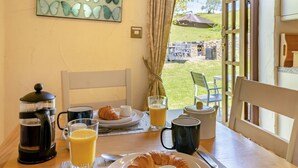 Une table de petit-déjeuner avec des croissants, du café et du jus d’orange, une vue sur un jardin et un tableau accroché au mur.