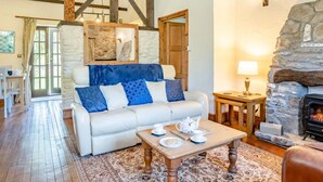 Un salon chaleureux avec un canapé blanc, une table basse en bois, une cheminée en pierre et un coin repas comprenant une table et des chaises.