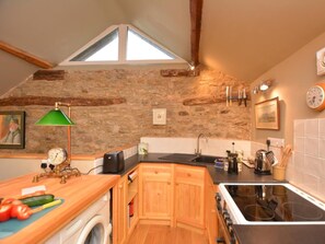 A kitchen with stone walls, wooden cabinets, a washing machine, a stove, and a sink.