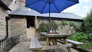 A stone building with a wooden door, a picnic table with benches, and a large blue umbrella.