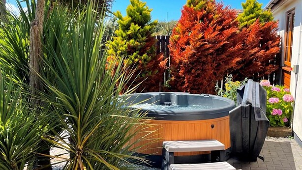Ein Whirlpool in einem Garten mit einer Holzterrasse, umgeben von verschiedenen Pflanzen und Bäumen.