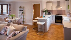 Eine moderne Küche mit Kochinsel, ein Essbereich mit rundem Tisch und ein Wohnzimmer mit Sofa und gemusterten Kissen.