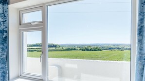 Ein Zimmer mit großem Fenster und Blick auf grüne Felder sowie ferne Hügel.