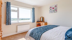 Ein Schlafzimmer mit großem Fenster, einem hölzernen Schminktisch, einem Bett mit blauer Bettdecke und einem Heizkörper.