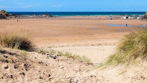 Ein weiter Sandstrand mit einem Leuchtturm in der Ferne, klarem Himmel und ruhiger See.
