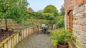 Une terrasse avec une table et des chaises, entourée d’une clôture en bois et d’un mur en briques.