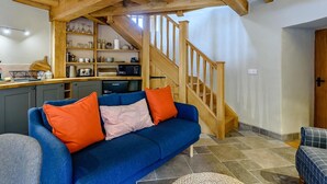 Un salon avec un canapé bleu, des poutres en bois, un coin cuisine et un escalier.