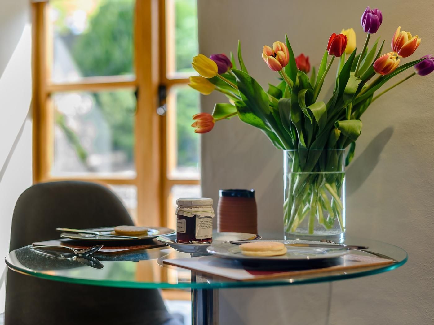 A glass table with a vase of tulips, a jar, and a plate with a cookie.