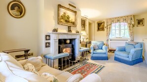 Ein traditionell eingerichtetes Wohnzimmer mit Kamin, zwei blauen Sesseln, einer Couch und einem gemusterten Teppich.