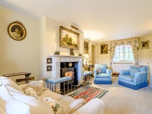 Ein traditionell eingerichtetes Wohnzimmer mit Kamin, zwei blauen Sesseln, einer Couch und einem gemusterten Teppich.