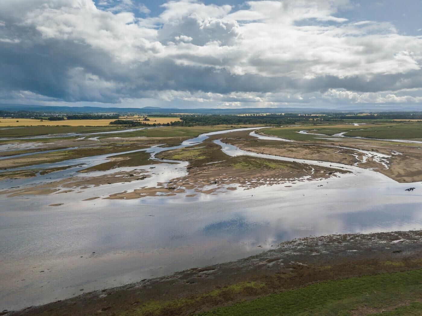 A river meandering through a flat landscape with distant hills and a cloudy sky.