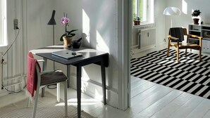 Une pièce comprenant un bureau, une chaise, des plantes en pot et un sol à carreaux noirs et blancs.