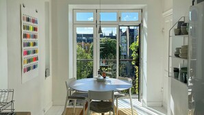 Une cuisine lumineuse avec une table à manger, des chaises, une grande fenêtre et une vue sur les bâtiments et la verdure environnante.