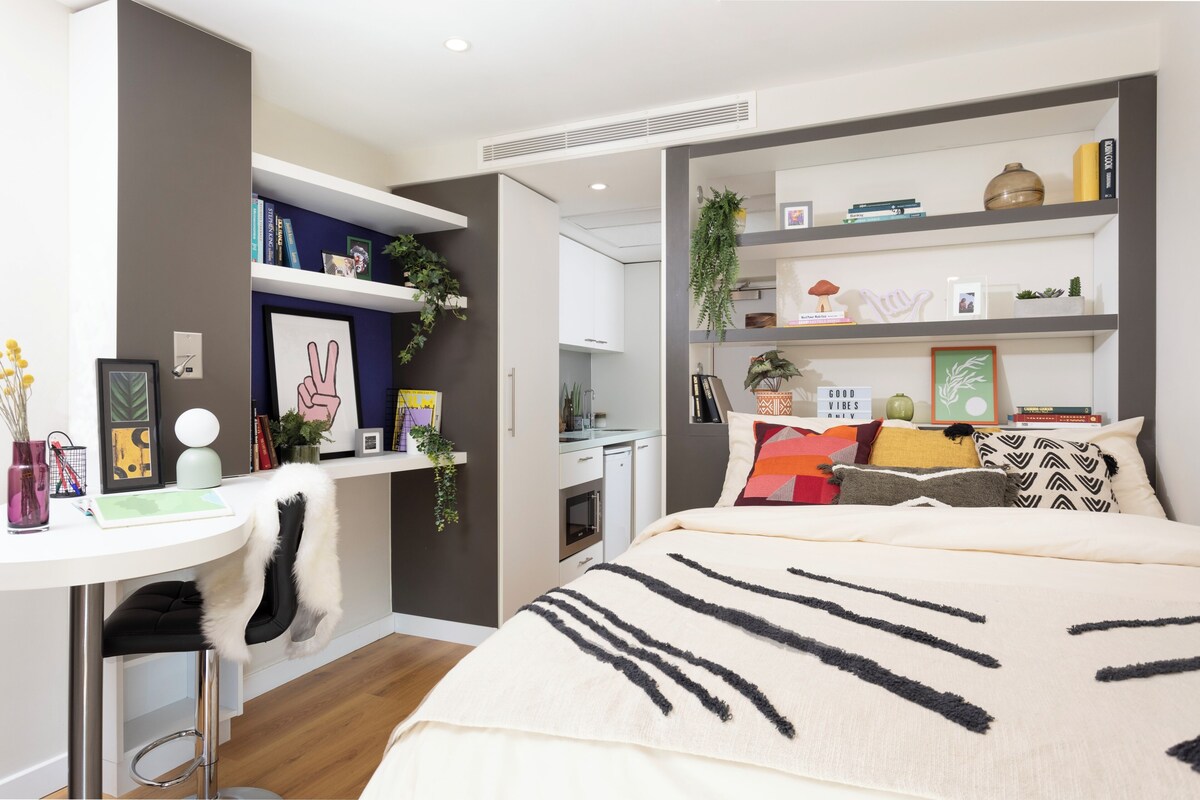 A modern bedroom with a bed, a desk, and a shelving unit.